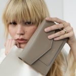 Aliso Handytasche in Taupe, von weiblichem Modell in einer Nahaufnahme vor dem Gesicht der Kamera gezeigt