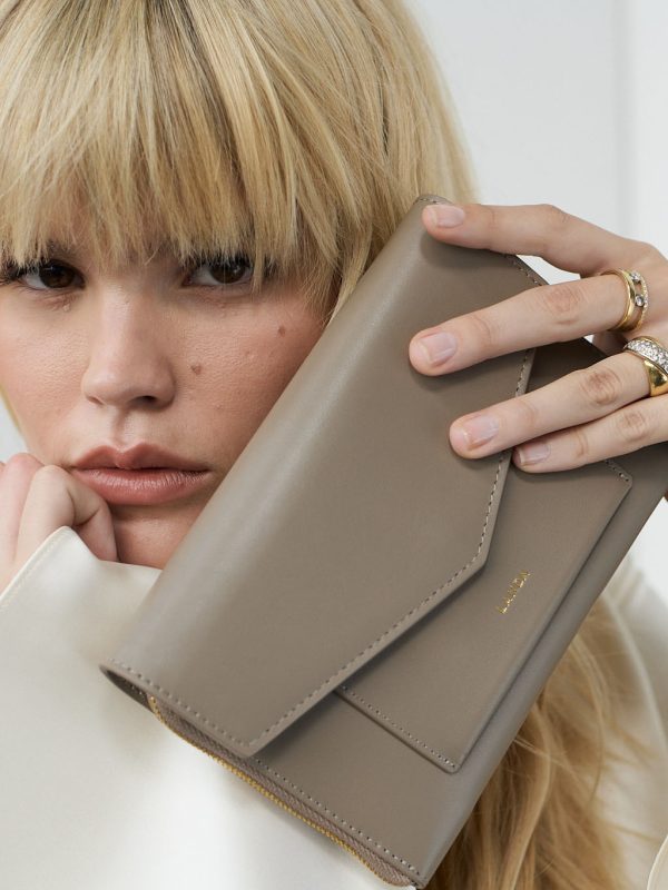 Aliso Handytasche in Taupe, von weiblichem Modell in einer Nahaufnahme vor dem Gesicht der Kamera gezeigt