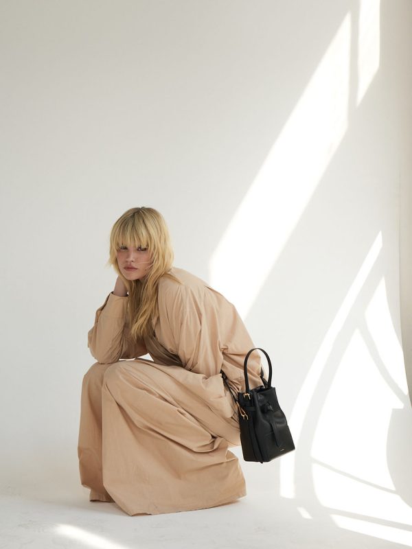 Baobab Bucket Bag in Schwarz, von weiblichem Modell in luftigem Kleid in Beige getragen