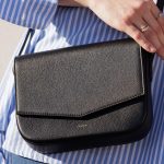 Olivo Umhängetasche in Schwarz, von weiblichem Modell in sommerlichem, weiss-blauem Kleid getragen