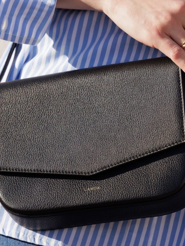 Olivo Umhängetasche in Schwarz, von weiblichem Modell in sommerlichem, weiss-blauem Kleid getragen