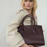 Palto City Bag in Burgunderrot, von weiblichem Modell in Businesskleidung mit Regenmantel in Crème unter dem Arm getragen