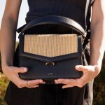 Teca Umhängetasche in Raffia, von weiblichem Modell in legerem Sommerkleid in Schwarz getragen