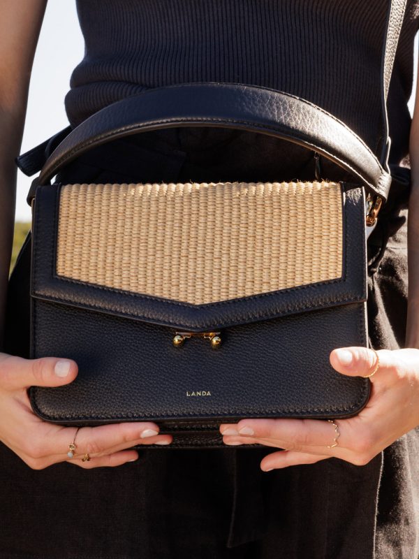 Teca Umhängetasche in Raffia, von weiblichem Modell in legerem Sommerkleid in Schwarz getragen