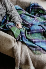 Decke aus Lammwolle «Connemara» - Violett, Blau und Grün, mit auf Sessel sitzender Person