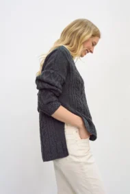 Aran-Pullover in Grau in Kastenform mit Seitenschlitzen. Weibliches Modell mit weissen Hosen trägt Aran Kastenpullover, Seitenansicht